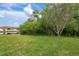 Lush green backyard with a view of a tranquil pond, bordered by trees and shrubs, under a blue sky at 19204 Weymouth Dr, Land O Lakes, FL 34638