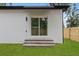 A white exterior wall with a sliding glass door and concrete steps leading to a grassy backyard at 7509 E 26Th Ave, Tampa, FL 33619