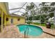 Backyard featuring a kidney shaped pool enclosed with a screen, brick pavers, and mature landscaping at 1051 Glynwood Pl, Dunedin, FL 34698