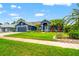 Inviting blue home with well-manicured lawn, colorful flowers, and palm trees under a clear sky, showcasing curb appeal at 28390 Openfield Loop, Wesley Chapel, FL 33543