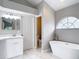 Luxurious bathroom with a soaking tub, modern fixtures, vanity, and arched window, offering a spa-like experience at 5809 Silas Creek Ln, Wesley Chapel, FL 33545