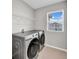 Well-lit laundry room with tile flooring, storage shelf, and Samsung washer and dryer at 32136 Conchshell Sail St, Wesley Chapel, FL 33545