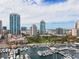 An aerial view showcases boats docked at a marina with luxurious condominiums against a backdrop of a vibrant city skyline at 100 Beach Ne Dr # 301, St Petersburg, FL 33701