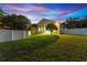 Backyard at dusk with large grassy area, white fencing, and covered patio outside of a beautiful home at 10310 Carroll Cove Pl, Tampa, FL 33612