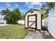 Backyard storage shed with a stained door and grassy area bordered by a white privacy fence at 12306 91St Ter, Seminole, FL 33772