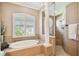 A tiled bathroom featuring a soaking tub, walk-in shower with glass door, and a decorative window shutter at 16248 Ivy Lake Dr, Odessa, FL 33556