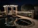 Elegant outdoor pool and hot tub with stone accents, illuminated pergola, and wrought iron fence at 16248 Ivy Lake Dr, Odessa, FL 33556