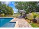 Backyard pool area featuring a large in-ground pool, patio with lounge chairs and umbrella, and landscaped garden at 13722 Lakemont Dr, Hudson, FL 34669