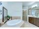 A luxurious bathroom featuring an oval soaking tub, glass-enclosed shower, and tiled vanity with modern fixtures at 1411 Tessano Pl, Palm Harbor, FL 34683