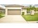 Beige single-story home featuring a two-car garage, palm trees, and a driveway at 16623 Carlton Pond St, Wimauma, FL 33598
