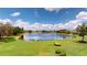 Expansive lake view, showing well-manicured green lawn and tropical trees, beneath a vibrant sky with puffy clouds at 9800 Sago Point Dr, Seminole, FL 33777