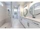 Modern bathroom features dual vanity, round mirrors, and a tiled shower, plus view into walk-in closet at 10308 Malvasia Ave, Riverview, FL 33578