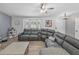 Bright living room featuring a gray sectional couch, bay window, and stylish ceiling fan at 5926 Frontier Dr, Zephyrhills, FL 33540