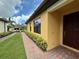 Inviting yellow home exterior with brick walkway, dark brown front door, and manicured garden beds at 21008 Fetterbush Pl, Venice, FL 34293