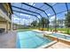 Sparkling screened-in pool with spa and lake views, surrounded by lush greenery and outdoor seating at 2566 Lake Manor Dr, Land O Lakes, FL 34639