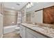 Bathroom featuring double vanity, granite countertops, modern fixtures, shower-tub, and wooden sliding door at 7570 Sweeter Tide Trl, Wesley Chapel, FL 33545
