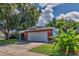 Side exterior view showing a red brick home with a two-car garage and lush trees at 13029 111Th Ln, Largo, FL 33778