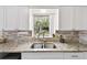 Bright kitchen with stainless steel sink, speckled granite countertops, white cabinets, and a window overlooking the yard at 1707 Cardinal Dr, Clearwater, FL 33759