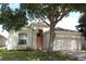 Beige single-story home featuring mature landscaping, arched entry, and a two-car garage at 221 Fairmont Dr, Spring Hill, FL 34609