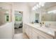 Bright bathroom featuring dual sinks with white cabinets, a glass-enclosed shower, and a view into the bedroom at 13157 Peachleaf Ave, Riverview, FL 33579