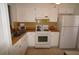 Galley style kitchen featuring white cabinets, matching appliances, and a yellow tile backsplash at 1406 Arrowhead W Cir, Clearwater, FL 33759