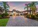 Elegant home featuring a grand entrance, arched windows, a paver driveway, and lush palm trees creating a tropical oasis at 9712 Tree Tops Lake Rd, Tampa, FL 33626