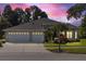 Charming home featuring a well-manicured lawn, mature trees, and a three-car garage at twilight at 10751 Tavistock Dr, Tampa, FL 33626