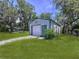 Exterior view of metal garage with roll-up door, side door, and lush green lawn and trees at 1861 Royal Oak E Pl, Dunedin, FL 34698
