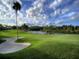 Scenic view of a lush golf course with a sand trap, framed by a calm lake and blue sky at 1861 Royal Oak E Pl, Dunedin, FL 34698