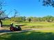 Beautiful golf course featuring a golf cart, lush green fairways, and mature trees under a clear blue sky at 1861 Royal Oak E Pl, Dunedin, FL 34698