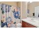 Bathroom with floral shower curtain, cherry vanity, and light tile flooring providing a functional and bright space at 19418 Butterwood Ln, Lutz, FL 33558