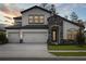 The home has a stone-accented entrance, a three-car garage, and a neatly landscaped front yard at dusk at 3458 Yellow Leaf Cir, Spring Hill, FL 34609