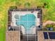 Aerial view of a screened pool with a spa, surrounded by lush landscaping and solar panels at 7244 Wild Oak Ln, Land O Lakes, FL 34637
