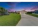 Exterior view of a single-story home at dusk featuring manicured lawns, mature trees, and a driveway to the two-car garage at 1414 75Th Nw St, Bradenton, FL 34209