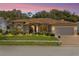 Charming single-story home at dusk featuring a well-manicured lawn, arched windows and a brick-paved driveway at 14228 Teasdale Ave, Hudson, FL 34667