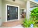 Inviting front porch featuring a dark wood door, brick flooring, and a cozy wicker chair at 17342 Lawn Orchid Loop, Land O Lakes, FL 34638