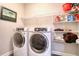 Laundry room with white washer and dryer, shelving, and a framed print at 2487 Golden Pasture Cir, Clearwater, FL 33764