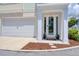 Inviting front entrance with a white door, lush landscaping, and a two-car garage for convenient parking at 803 Oak Bend Ln, Dunedin, FL 34698