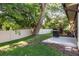 Grassy backyard featuring a white fence line, mature trees, and a concrete patio with a grill at 1380 Azalea Dr # 1701, Dunedin, FL 34698
