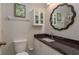 This bathroom features a granite countertop, decorative mirror and white cabinets for storage at 1380 Azalea Dr # 1701, Dunedin, FL 34698