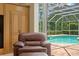 Armchair close to a sliding door with a view of the swimming pool and green vegetation outside at 17818 Arbor Greene Dr, Tampa, FL 33647