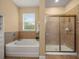 Bright bathroom featuring a tiled shower, soaking tub under a window, and tan walls at 27546 Stonecreek Way, Wesley Chapel, FL 33544