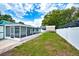 View of the home's backyard, featuring a screened lanai, grassy area, and a white privacy fence at 17824 Morninghigh Dr, Lutz, FL 33549