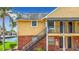 Exterior shot of a yellow condo building with brick foundation and stairs leading to the second floor entrances at 200 Country Club Dr # 202, Largo, FL 33771