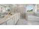 Bright bathroom features dual sinks, a glass shower, and a separate soaking tub under a window at 2328 Stratten Dr, Zephyrhills, FL 33541