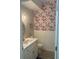 Stylish powder room featuring a white vanity with marble countertop and floral wallpaper at 1050 Starkey Rd # 106, Largo, FL 33771