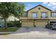 Two-story tan townhome featuring dual car garages, a small balcony, and verdant landscaping at 27563 Pleasure Ride Loop, Wesley Chapel, FL 33544