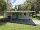 Simple mobile home with a covered carport, a vibrant turquoise door, and lush green surroundings at 5105 Wood St, Zephyrhills, FL 33542