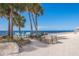 Two benches sit on a white sand beach with clear blue water in the background surrounded by palm trees at 6340 Garland Ct, New Port Richey, FL 34652
