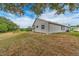 A grey single-story home features a spacious backyard under a blue sky with scattered clouds at 921 Linn Harbor Ct, Tarpon Springs, FL 34689